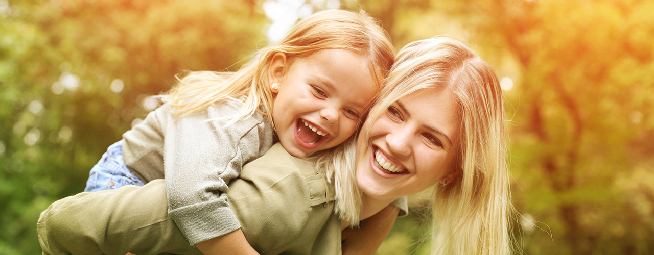 Laughing young daughter on a piggy back ride with her mother